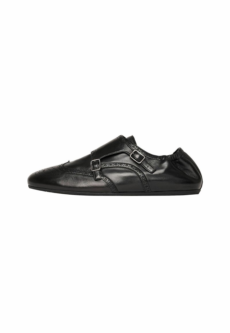 Scarpa in pelle nera dal design elegante, con perforazioni decorative, due cinturini con fibbie e suola piatta. Retro morbido ed elasticizzato per un maggiore comfort.