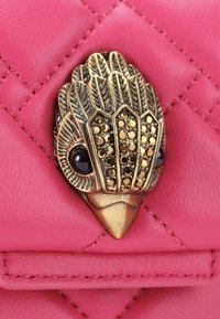 Bolso de cuero acolchado rosa con un cierre en forma de pájaro metálico que presenta acentos negros y adornos dorados en el cuerpo y la cabeza.