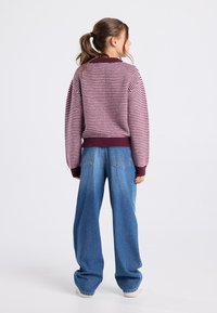 Violetti ja vaaleanpunainen raidallinen neulepaita, jossa on ribbaus kauluksessa ja hihoissa, yhdistettynä väljään vaaleansiniseen farkkuun. Asusteessa on rento istuvuus.