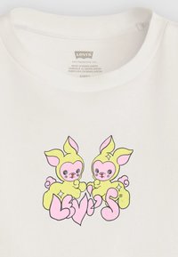 T-shirt en coton blanc arborant un design graphique de deux lapins en cartoon en jaune et rose, avec le texte "Levi’s" intégré en dessous.