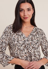 Blusa a maniche lunghe con sfondo bianco e motivo a foglie nere e arancioni, scollatura a V e polsini con bottone. Tessuto leggero.