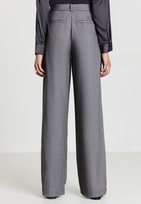 Persona che indossa pantaloni larghi a righe grigie con vita alta e una camicia a maniche lunghe in satin scuro, vista da dietro.