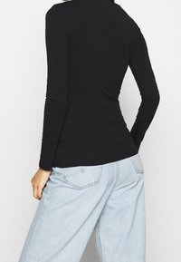 Svart långärmad topp med en figurnära design, slät textur och diskret sömnadsdetalj, i kombination med ljusblå löst sittande jeans.