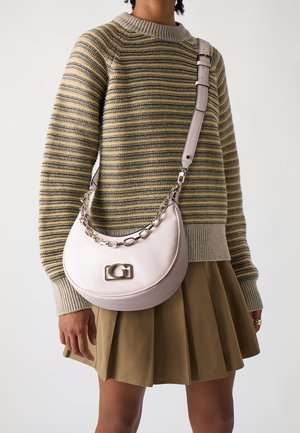 Personne portant un pull en maille rayé et une jupe plissée olive, tenant un sac à main croissant rose clair avec une chaîne et une boucle dorées.