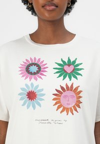 Weißes Baumwoll-T-Shirt mit einem bunten grafischen Druck von Blumen und einer Sonne, mit detaillierten Formen und Texturen in Pink, Blau, Grün und Braun.
