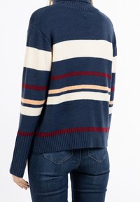 Laivastonsininen neulepusero, jossa on resorikaulus. Siinä on vaakasuoria raitoja, jotka ovat väriltään kerma, punainen ja beige. Pehmeä pinta, rento istuvuus.