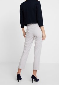 Top cropped blu navy sopra pantaloni grigi chiari fitted con cuciture laterali. Modella in tacchi alti blu scuro, in piedi contro uno sfondo neutro.