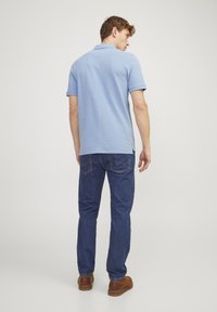 Hellblaues Polohemd mit kurzen Ärmeln, getragen mit dunkelblauen Jeans und braunen Schuhen, von hinten betrachtet. Einfaches Design mit gerader Form.