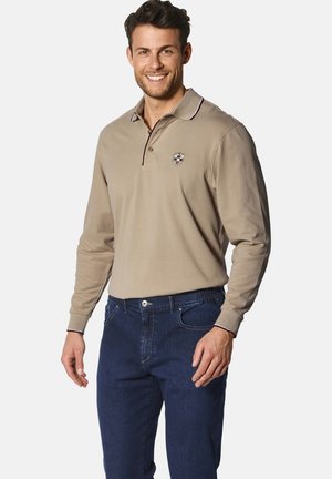 Beige Langarm-Polo mit einer Knopfleiste mit zwei Knöpfen und dunkelroten Akzenten, kombiniert mit dunkelblauen Jeans aus Denim mit vorderen Taschen und Nähdetails.