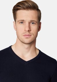 Granatowy sweter w serek z dzianiny, z delikatnym logo na lewej piersi oraz ściągaczem przy dekolcie dla tekstury i detalu.