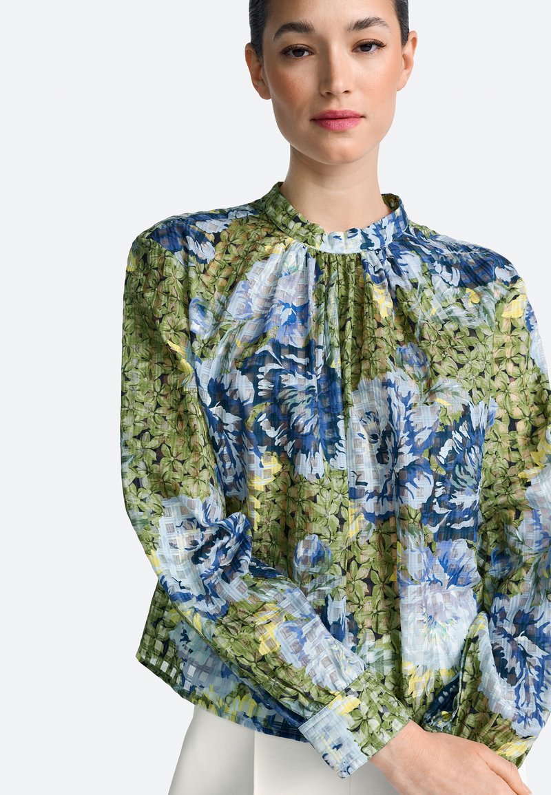 Bluza florală dintr-un material ușor, transparent, cu nuanțe de albastru și verde, decolteu adunat și mâneci lungi cu detalii la manșetă.