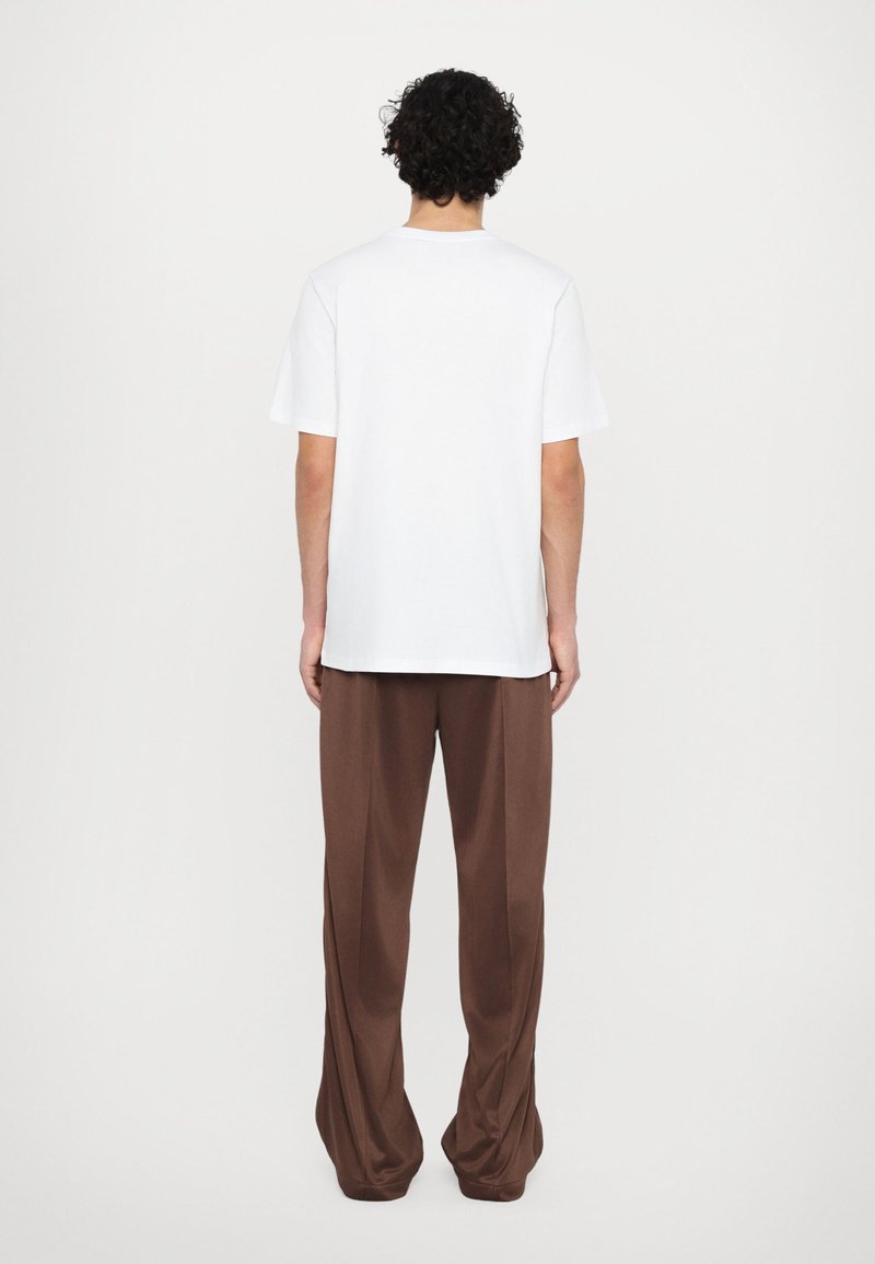 Hvid bomulds T-shirt og brune afslappede bukser. T-shirten har en rund halsudskæring, og bukserne har en glat, flydende tekstur og brede ben.