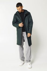 Tummanvihreä sadeviitta hupulla, pitkät hihat ja etuvetoketju. Päällä musta neule, yhdistettynä vaaleanharmaisiin farkkuihin ja valkoisiin tennareihin.