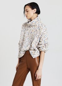 Pullover lavorato a maglia in crema con macchie multicolori, caratterizzato da un collo alto, una vestibilità rilassata e una texture a costine, abbinato a pantaloni di pelle marrone.