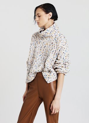 Knitpullover in Creme mit mehrfarbigen Sprenkeln, ausgestattet mit einem hohen Kragen, lässiger Passform und gerippter Textur, kombiniert mit braunen Lederhosen.