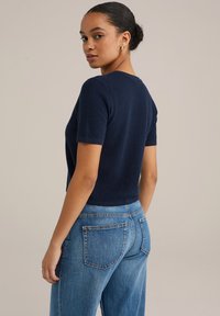 Tumedat sinine kootud lühikeste varrukatega topp ümmarguse kaelustega; sobitatud helesiniste kõrge talje pitsidega teksadega; sile tekstuur ja sobiv disain.