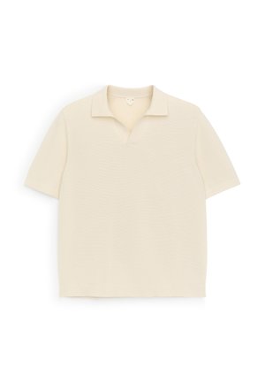 Polo en maille crème à manches courtes avec col et petite ouverture en V, posé à plat sur un fond blanc.