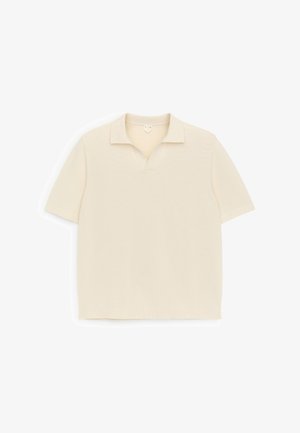 Polo en maille crème à manches courtes avec col et petite ouverture en V, posé à plat sur un fond blanc.