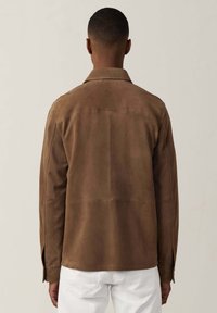 Giacca in suede marrone con una vestibilità rilassata, caratterizzata da un colletto a punta, maniche lunghe e una texture liscia. Dettagli di cucitura sulla parte posteriore.