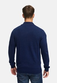 Granatowy sweter dzianinowy z prążkowanym kołnierzem i mankietami. Klasyczny krój, średnia grubość, fakturowana tkanina. Nosi się z dżinsami.