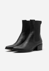 Černé kožené kotníkové boty s špičatou špičkou, elastickými postranními panely a masivním podpatkem. Hladký povrch a elegantní design.