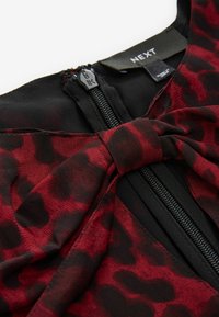 Roter und schwarzer Leopardenmuster-Kleidstoff mit Schleifendetail an der Taille, mit einem zentralen Reißverschluss und weicher Textur. Markenetikett sichtbar.