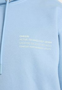 Világoskék kapucnis pulóver puha, texturált anyagból. Elöl fehér szöveges nyomattal, amelyen az "ACTIVE-TECHNOLOGY-DENIM" felirat olvasható.