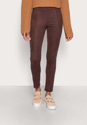 As leggings de imitação de camurça cor burgundy apresentam uma cintura alta, ajuste justo e costuras laterais subtis. Combinadas com ténis de tiras duplas em tom bege claro.