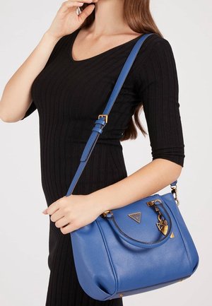 Sac en cuir bleu avec une forme structurée, accents en matériel doré et une courte poignée, présenté sur un fond neutre.