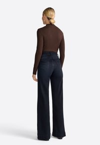 Braunes, eng anliegendes Langarmoberteil, kombiniert mit hoch taillierten, dunkelblauen, weiten Jeans. Die Hose hat ein klassisches Fünf-Taschen-Design und Saumdetails.