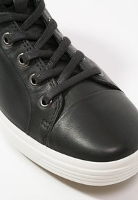 Schwarze Leder-Sneaker mit gerundetem Zehenbereich, metallischen Ösen und schwarzen Schnürsenkeln sowie einer weißen Gummisohle mit strukturierten Details.