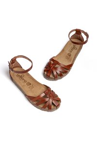 Sandali in pelle marrone con cinturini incrociati, fibbia alla caviglia e soletta ammortizzata. Suola piatta con un design del pattino a motivi.