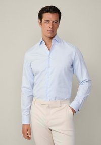 Lichtblauw geblokt overhemd met lange mouwen, witte knopen en contrasterende manchetten, gecombineerd met beige op maat gemaakte stofbroek.