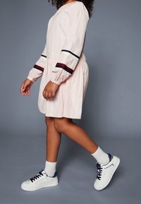 Vaaleanpunainen mekko pitkilla hihoilla, jossa on punaisia, mustia ja valkoisia raitoja; yhdistetty valkoisiin tennareihin ja nilkkasukkien kanssa. Sujuva pinta.