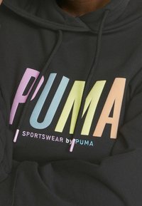 Sweat à capuche noir avec cordon de serrage. Présente un grand texte "PUMA" multicolore et le logo "SPORTSWEAR by PUMA" avec des accents rose, blanc et bleu.