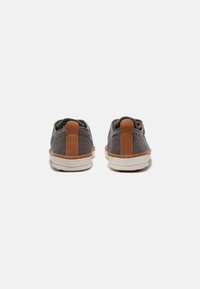 Szare buty z tkaniny o fakturowanym wykończeniu, z brązowym skórzanym uchwytem na pięcie i białą gumową podeszwą. Klasyczny design z minimalnymi detalami.