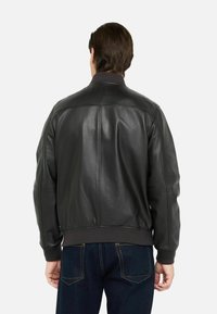 Giacca bomber in pelle nera con colletto e polsini a coste, caratterizzata da una texture liscia, spalle strutturate e un design semplice.