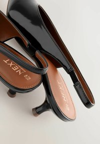Mustat patenttinaamio slingback-korkokengät, joissa on terävä kärki, 5 cm kitten-korko ja vaaleanruskea pohja, jossa on kohokuvioitu "NEXT"-logo.