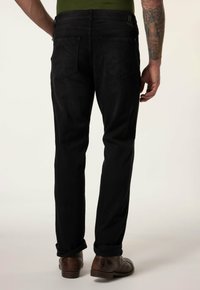 Jeans de mezclilla negros con corte recto, con una altura media, bolsillos traseros y una textura sutil. Combinados con zapatos marrones.