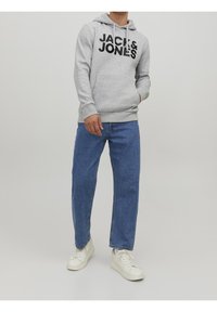Šedá mikina s kapucí s černým logem "JACK & JONES", vybavená klokaní kapsou a stahovací kapucí, v kombinaci s modrými rovnými džínami a bílými teniskami.