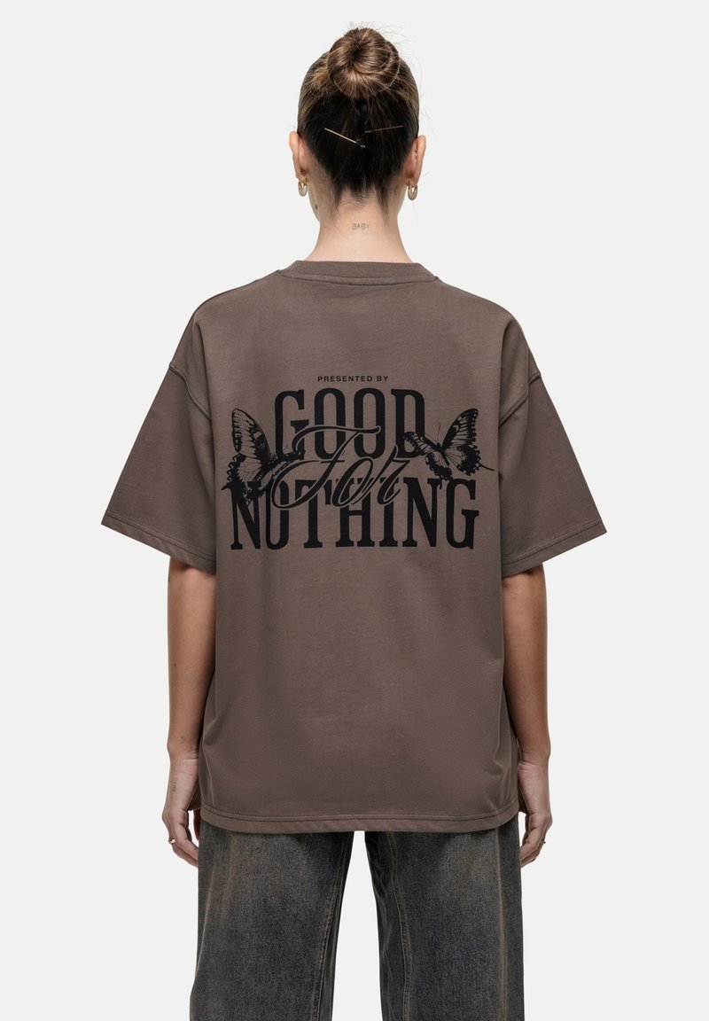 Bruine oversized t-shirt met een gedurfde zwarte graphic op de achterkant, versierd met vlinderaccenten en de tekst "PRESENTED BY GOOD FOR NOTHING."
