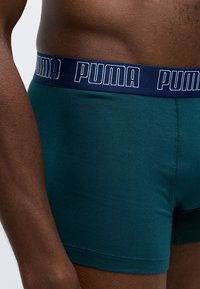 Tengeri kék boxeralsó, puha anyagból készült, navy színű elasztikus derékpánttal, amelyen fehér "PUMA" logó található, és testhezálló fazonú.