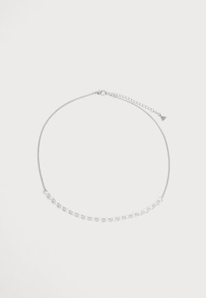 Collier chaîne en argent avec une petite partie reliée à l'avant et un fermoir réglable sur un fond uni et clair.