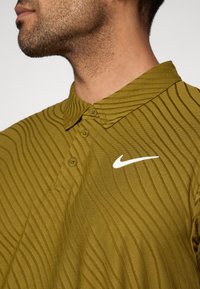 Πράσινο πόλο πουκάμισο Nike με γιακά, με υφή κυματιστού μοτίβου, διαθέτει λευκό λογότυπο στο επάνω αριστερό μέρος και κουμπιά στον γιακά.