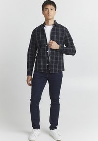 Camisa de cuadros en blanco y negro con cuello abotonado, llevada sobre una camiseta blanca. Combinada con jeans oscuros y zapatillas blancas.