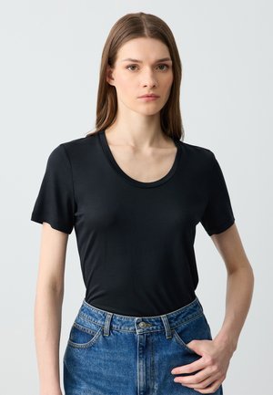 T-shirt nera a maniche corte con scollatura rotonda, realizzata in tessuto morbido. Abbinata a jeans in denim blu a vita alta.