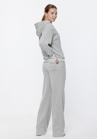 Szary zestaw z hoodie i dresami wykonany z miękkiego, rozciągliwego materiału. Posiada kaptur, kieszeń typu kangur i luźny krój z elastycznymi mankietami.