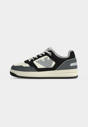Χαμηλό sneaker σε μαύρο, άσπρο και γκρι με κορδόνια στο μπροστινό μέρος και σχέδιο λογότυπου στην πλευρά, εμφανίζεται από την εξωτερική πλευρά σε λευκό φόντο.