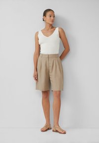 Débardeur blanc ajusté avec décolleté en V. Short beige plissé avec poches latérales. Sandales en or à brides. Design simple et minimaliste.