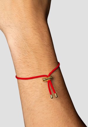 Red rope bracelet with a gold accent piece and two gold tipped ends, resting on a wrist, displaying a smooth skin texture.